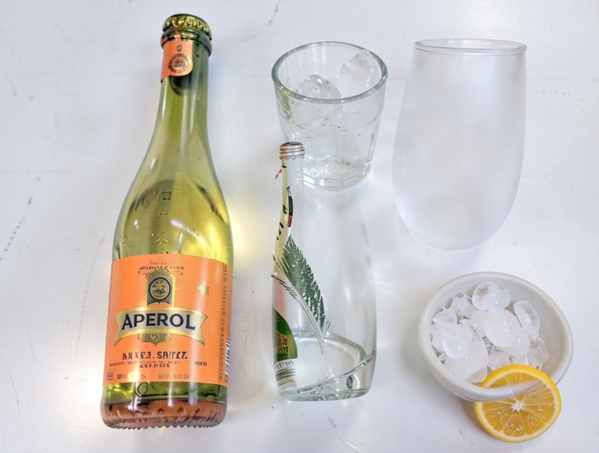 Flat lay of Aperol, Prosecco, club soda, cracked ice, and orange slice for a spritz