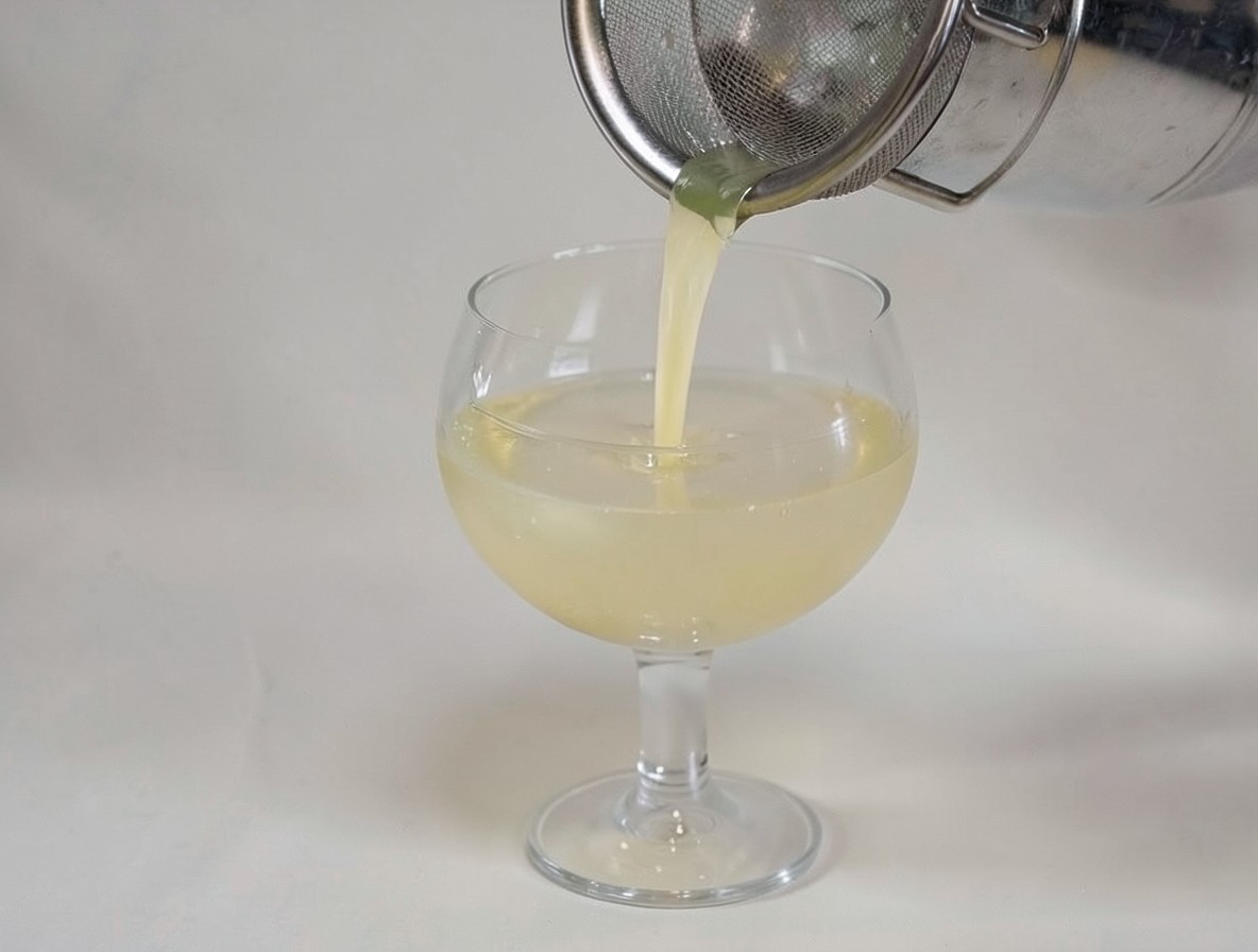 Straining the Bee's Knees cocktail through a fine mesh strainer