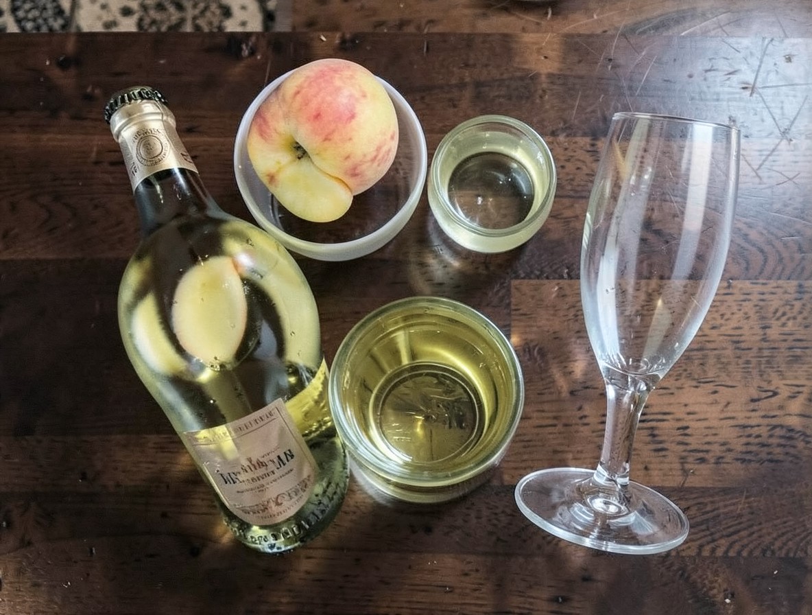 Flat lay of Bellini ingredients: white peach, Prosecco, lemon, and a flute