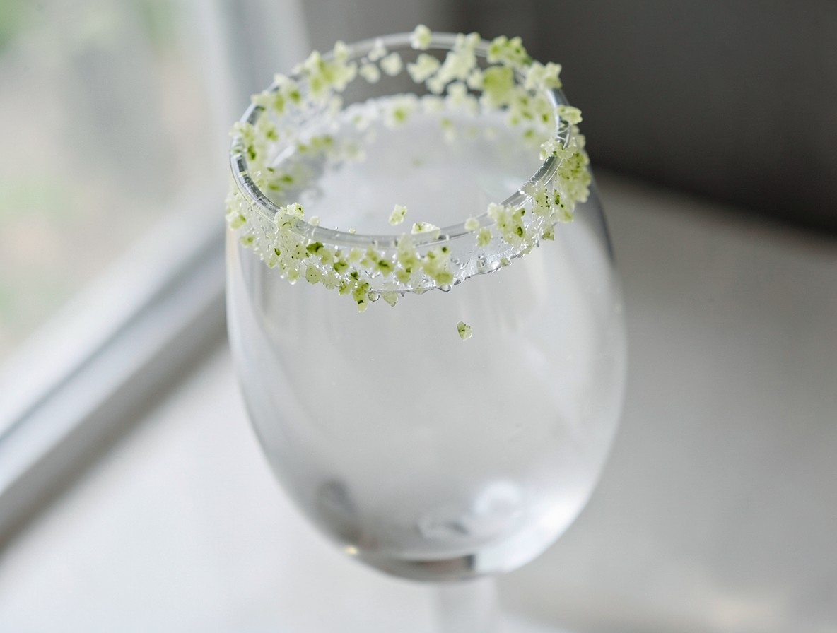 Close-up of celery salt being applied to the rim of a highball glass.