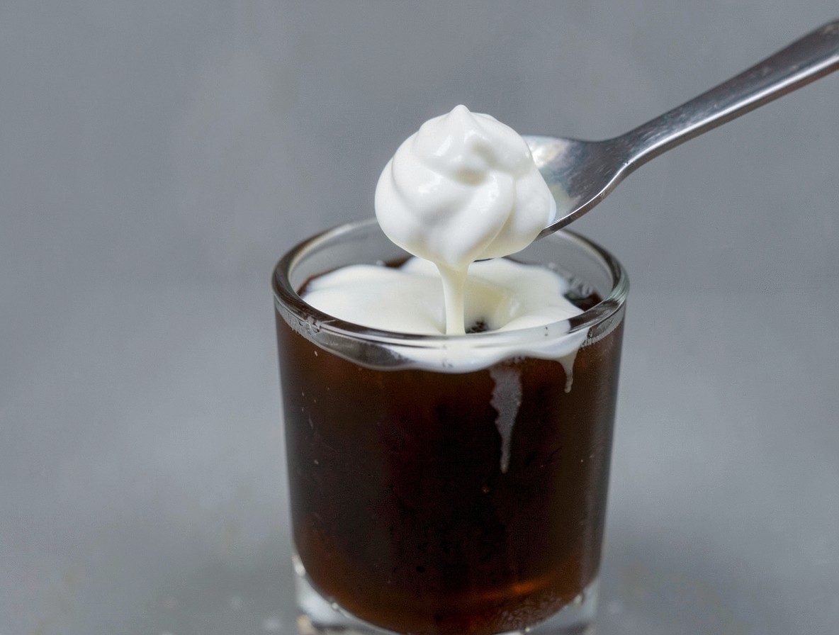 Pouring whipped cream over the back of a spoon onto Irish coffee