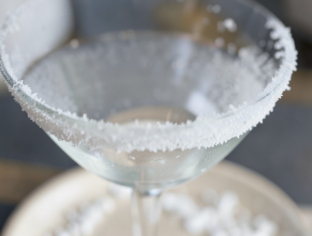 Close-up of sugar rims on a chilled martini glass with sugar scattered on a plate