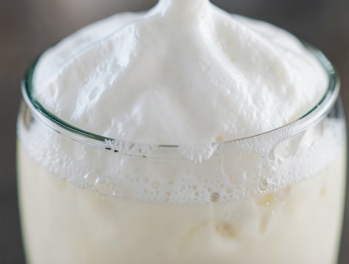 Macro shot of the thick, creamy foam head on a Ramos Gin Fizz rising above the glass rim