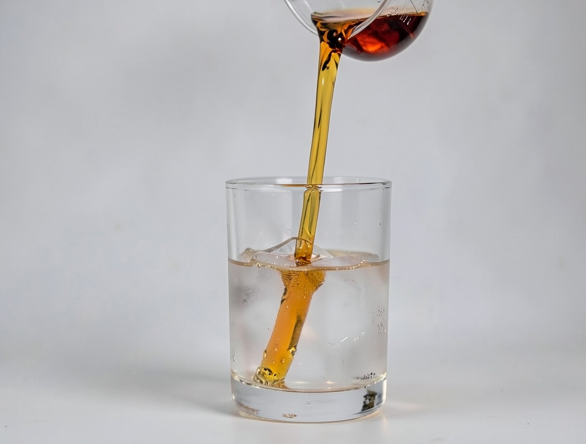 Pouring a strained rum old fashioned from a mixing glass over a large ice cube