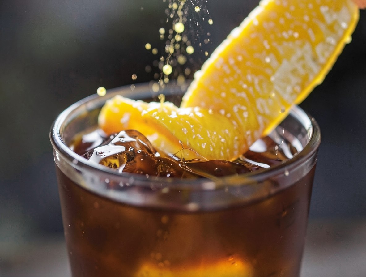 Expressing an orange twist over a rum old fashioned cocktail, citrus oils in the light