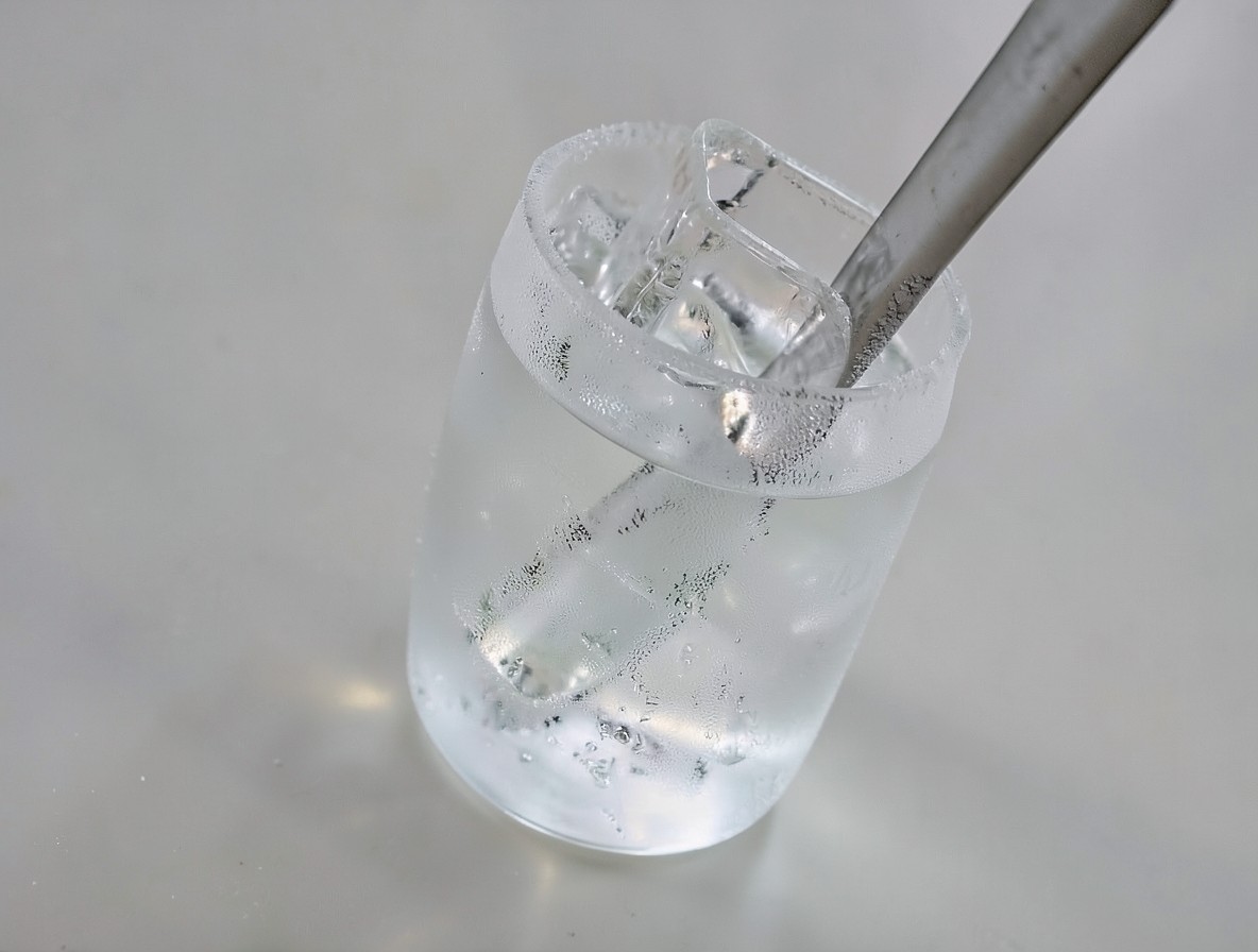 Mixing glass with clear spirits, ice, and bar spoon before stirring